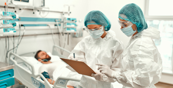 Two doctors with masks reading chart of patient laying in hospital bed.